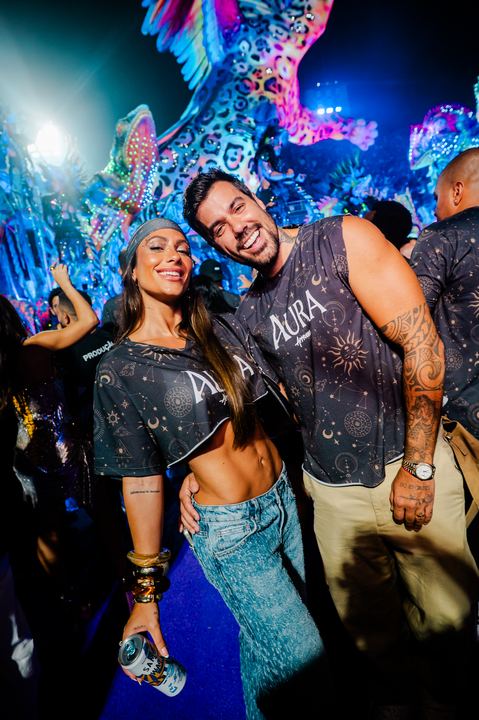 Casal no camarote com o carro alegórico ao fundo